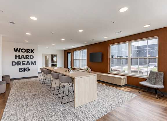 A room with a long table and chairs with a sign on the wall that says "work hard dream big".