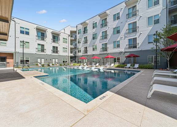A swimming pool surrounded by apartment buildings and lounge chairs.