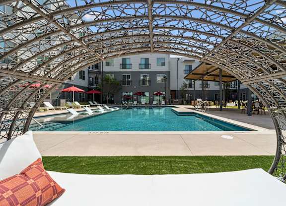 A pool surrounded by a white wall and a metal trellis.