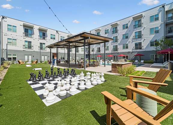 A giant chess board is set up on a lawn in front of apartment buildings.