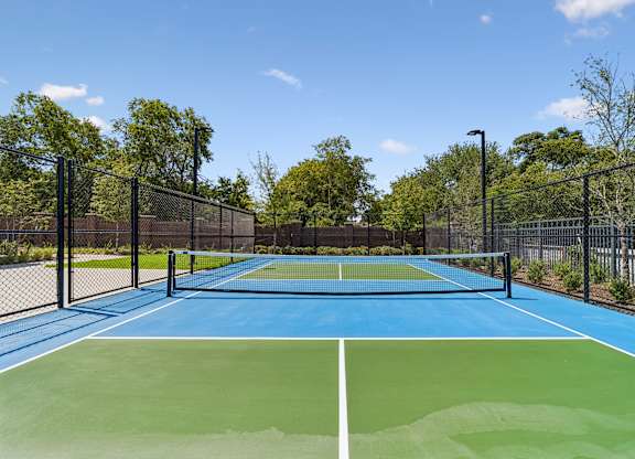 A tennis court with a blue and green surface surrounded by a black fence.