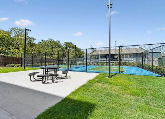 A tennis court surrounded by a fence with a picnic table in front.