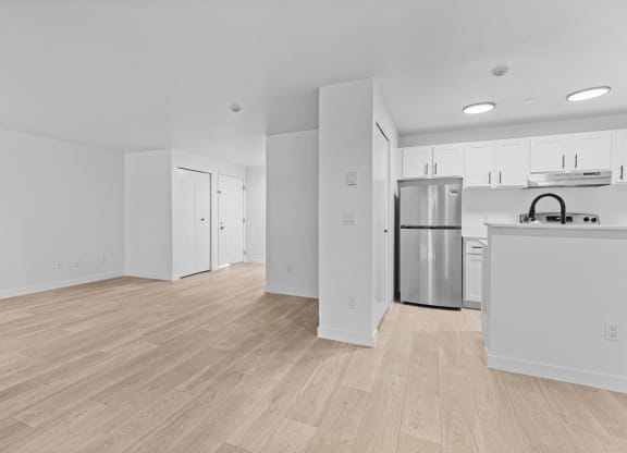 the living room and kitchen of an apartment with white walls and wood flooring