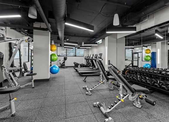 A gym with a variety of equipment including treadmills, weights, and exercise balls.