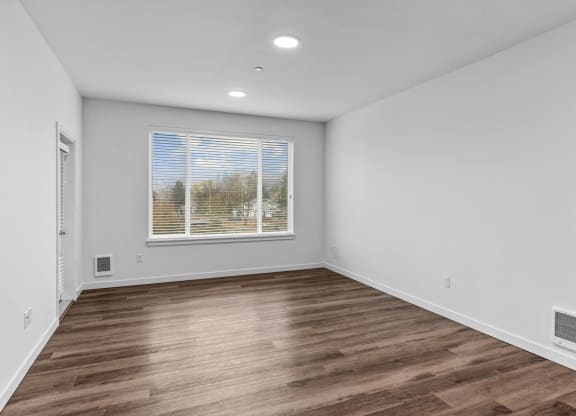 a living room with white walls and wood flooring and a window