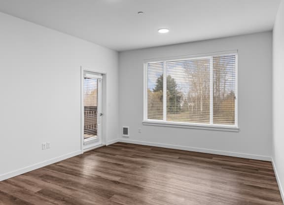 the living room of an apartment with a large window and wood flooring