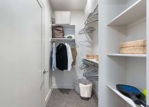 a small walk in closet with shelves and a closet door open to a white closet