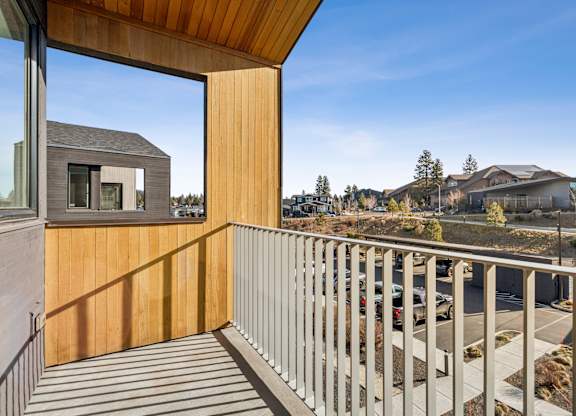 A balcony with a wooden railing and a view of a parking lot and buildings.
