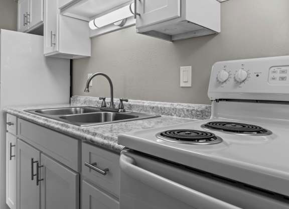 A white stove top oven with a silver sink and a white refrigerator in a kitchen.