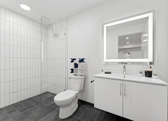 OnyxOnPark_SanDiego_CA_Model_1BR_ A white bathroom with a toilet, sink, and mirror.