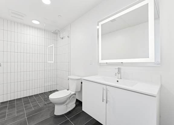 OnyxOnPark_SanDiego_CA_Vacant_2BR_ A white bathroom with a toilet, sink, and mirror.