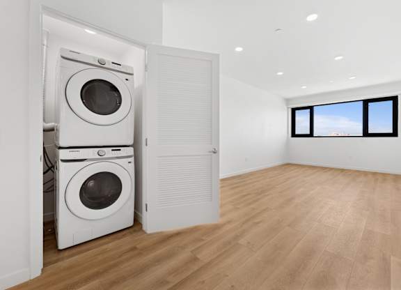 OnyxOnPark_SanDiego_CA_Vacant_2BR_ A white washing machine is in a room with wooden floors and a window.