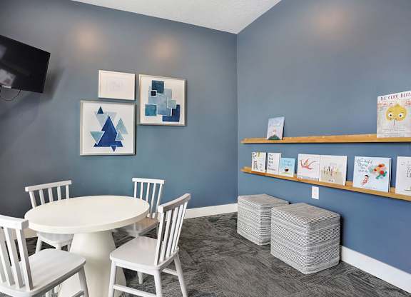 Alvera at the Meadows room with a white table and chairs, a TV, and some artwork  and books on the wall.