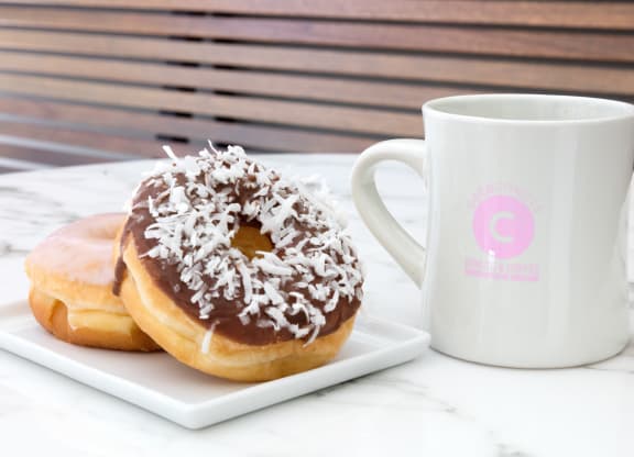 two donuts on a plate next to a coffee mug
