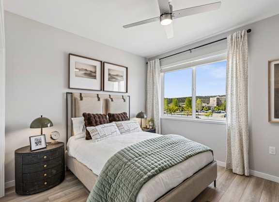 A bedroom with a large bed, a ceiling fan, and a view of the outdoors through a window.