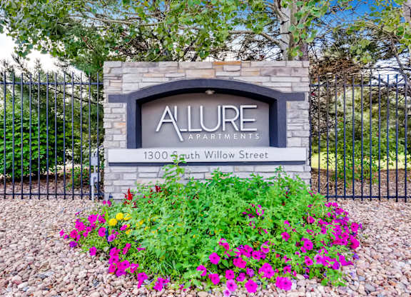 A sign that says Allure Apartments is in front of a black fence.