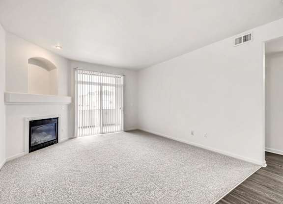 A large, empty room with a fireplace and a window with blinds.