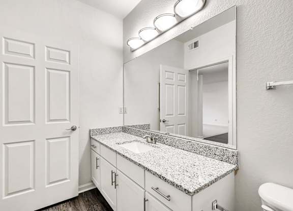 A bathroom with a granite countertop and white cabinetry.