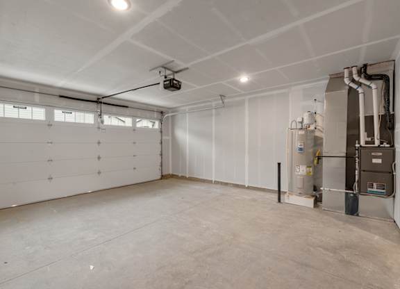 A large, empty room with a garage door on the left and a furnace on the right.