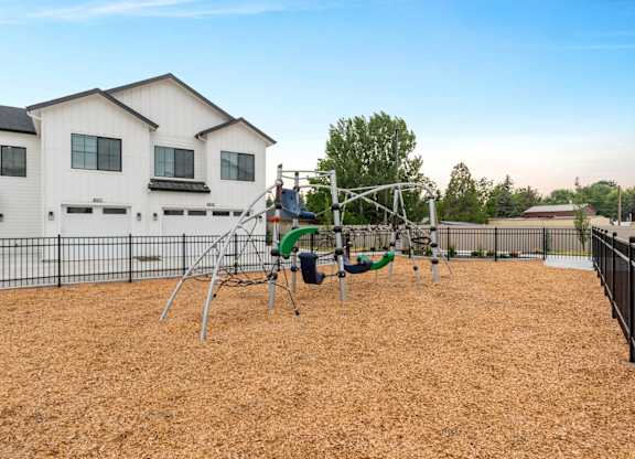 A playground with a swing set and a slide in front of a white house.