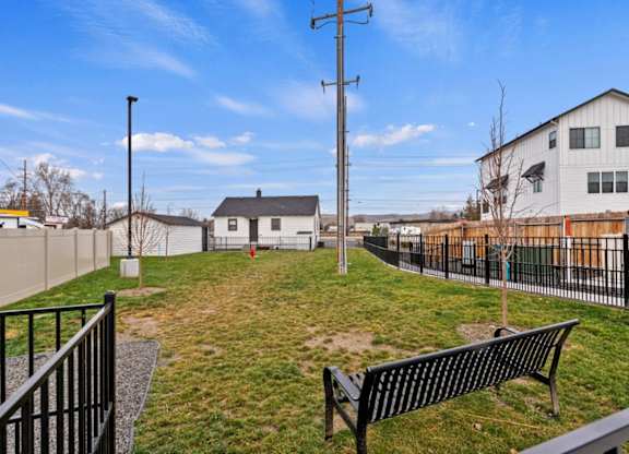 A black bench sits in a grassy area next to a fence.
