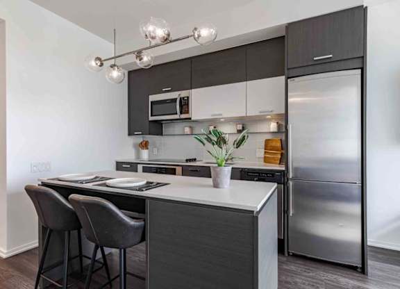 A modern kitchen with a stainless steel refrigerator, a black countertop, and a white backsplash.