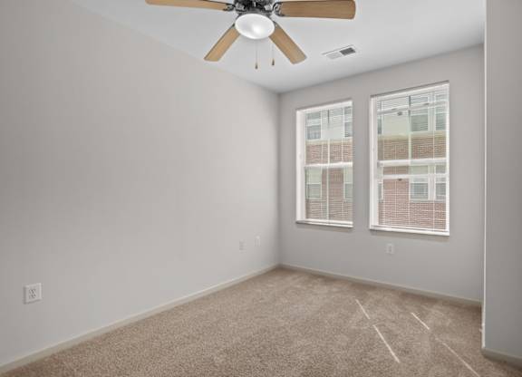 A room with a ceiling fan and two windows.
