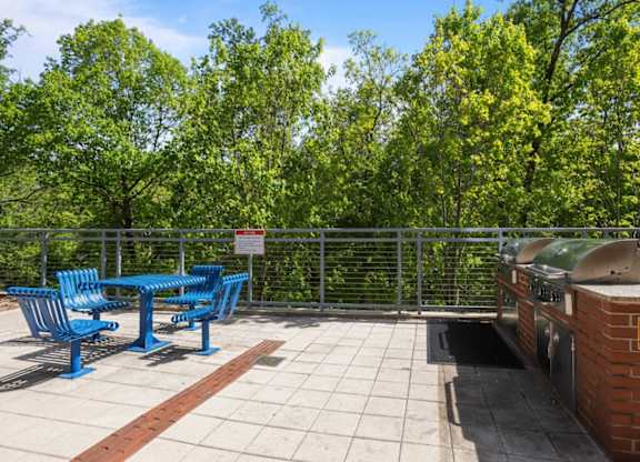 A blue table and chairs are on a patio with a brick wall and a trash can.