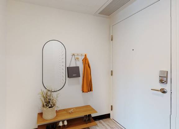 A white wall with a mirror, a bench, and a plant on it.