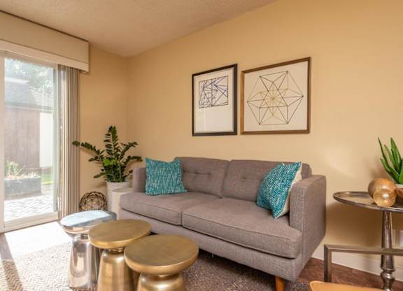 A grey couch with a blue pillow is in the middle of a room with two tables and two framed pictures on the wall.