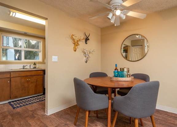 A dining room with a round mirror, a wooden table, and grey chairs.