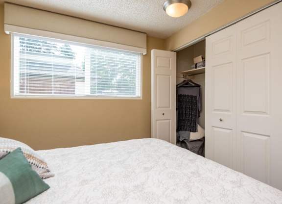 A bedroom with a bed, a window with blinds, and a closet.
