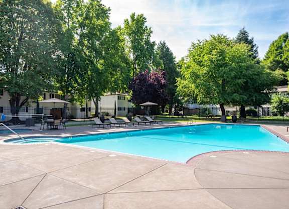 A large swimming pool surrounded by trees and chairs.