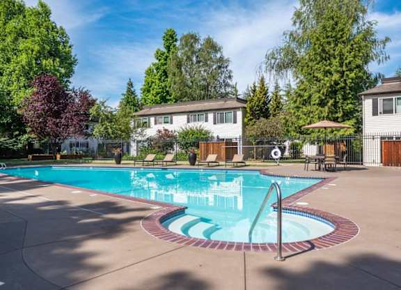 A large outdoor swimming pool surrounded by trees and a white building.