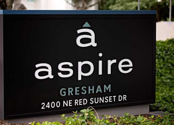 A black sign with white lettering that says "a aspire Gresham 2400 NE Red Sunset Dr".