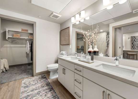 A bathroom with double white sink, toilet, and a mirror.