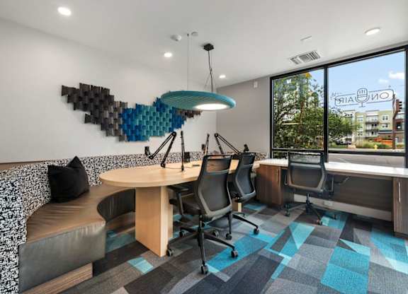 A modern office space with a wooden table and chairs, a patterned carpet, and a large window with a view of the city.
