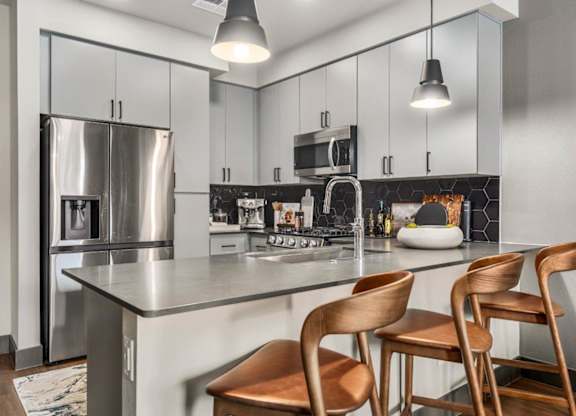 A modern kitchen with a stainless steel refrigerator, a stove, and wooden chairs.