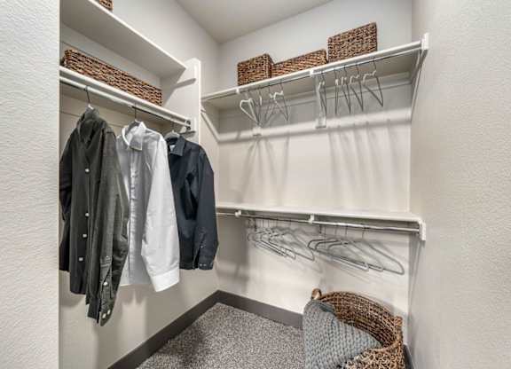 A white closet with clothes hanging and baskets on the shelf.