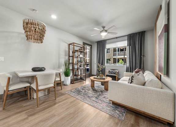 A living room with a white couch, a wooden dining table with chairs, a rug, and a ceiling fan.