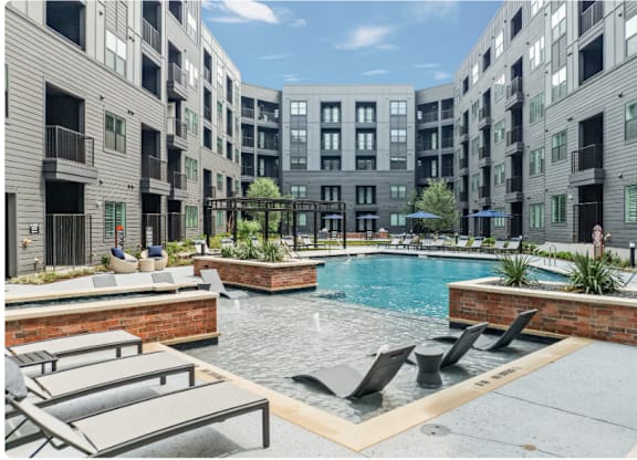 A pool surrounded by lounge chairs and planters in a courtyard.