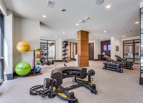 A gym with a variety of equipment including a rowing machine, exercise balls, and dumbbells.