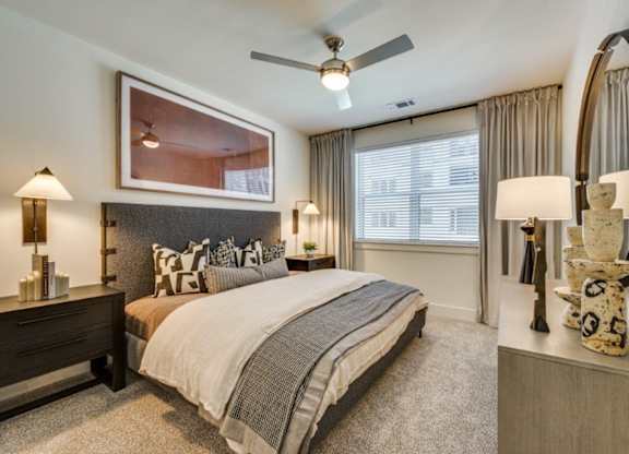A bedroom with a large bed, a ceiling fan, and a painting on the wall.