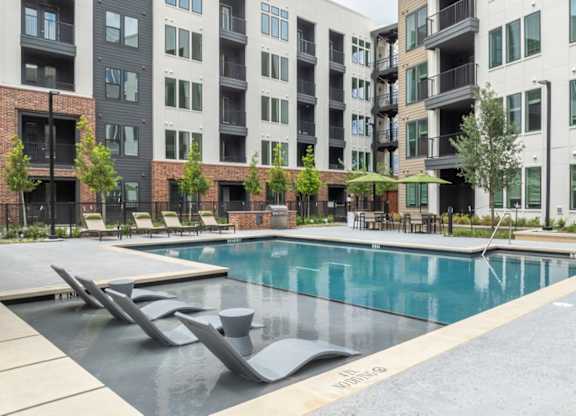 A swimming pool surrounded by modern buildings and lounge chairs.
