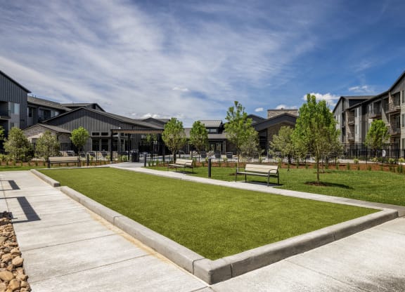 a park with green grass and benches in front of buildings
