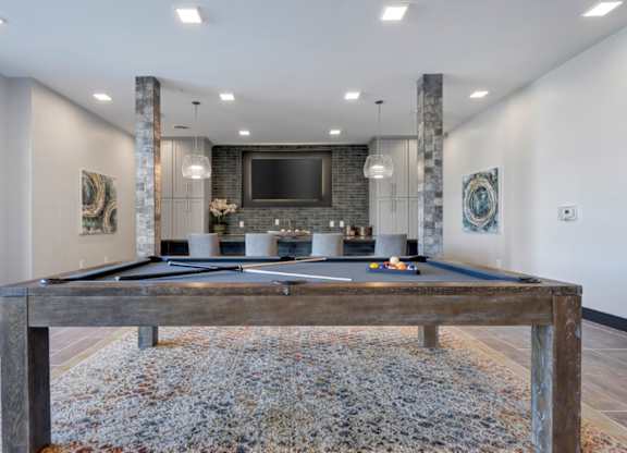 A pool table in a room with a stone pillar and a television mounted on the wall.
