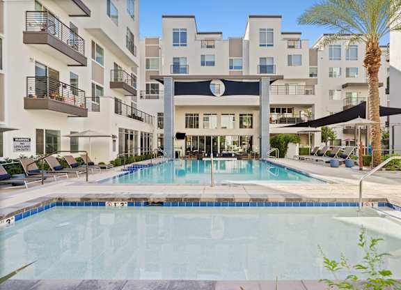 A swimming pool in front of a building with a palm tree.