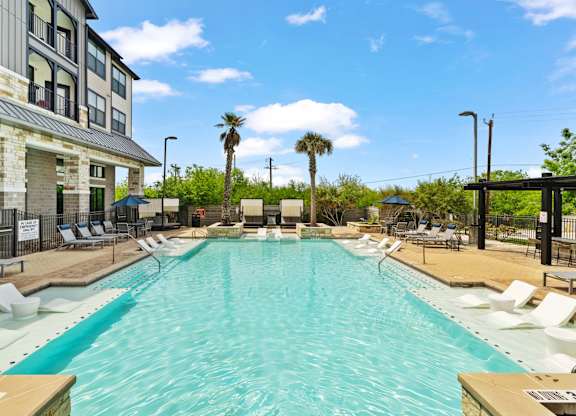 A large swimming pool with lounge chairs and palm trees in the background.