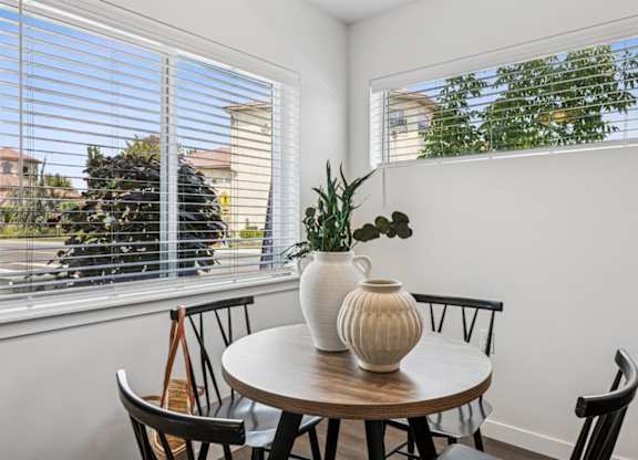 A table with a vase and a plant on it in front of a window.