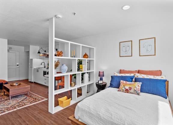a bedroom with white walls and a white bed with blue and orange pillows